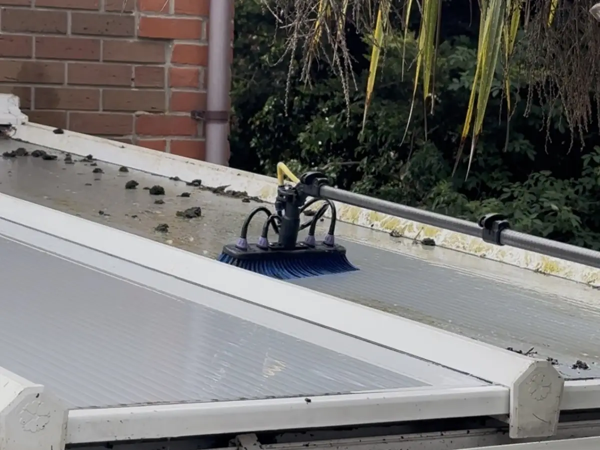 A brush on a pole cleaning a conservatory roof covered in leaves