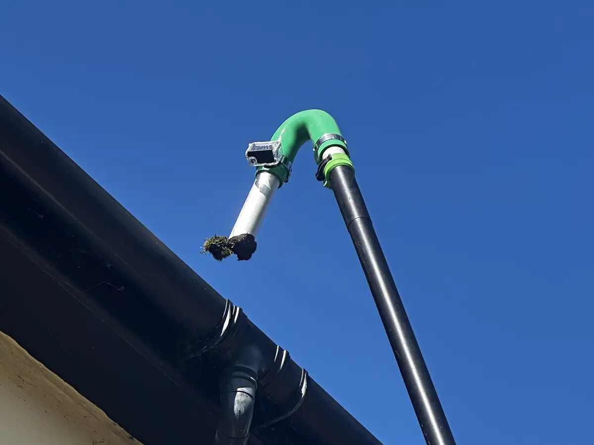 The gutter vacuum's pole and camera reaching over a black gutter against a blue sky