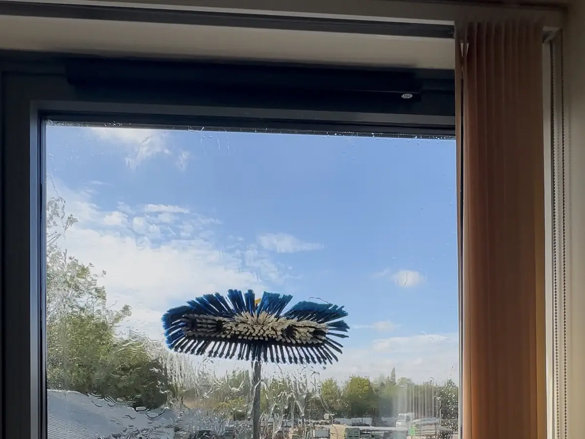 A pure-water brush on a long pole cleaning an upstairs window, seen from inside