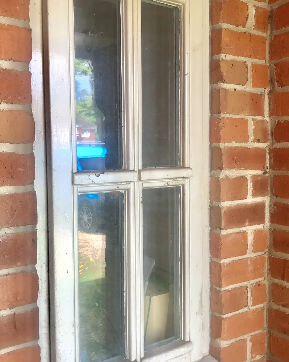Before: a white-painted window on red brick with grubby glass and frames