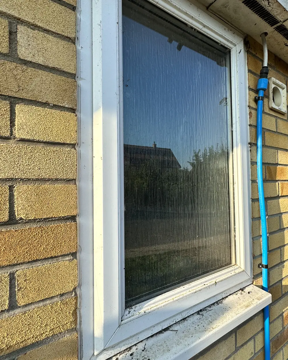 Before: a white window on a yellow-brick wall with spotty glass and a dirty sill